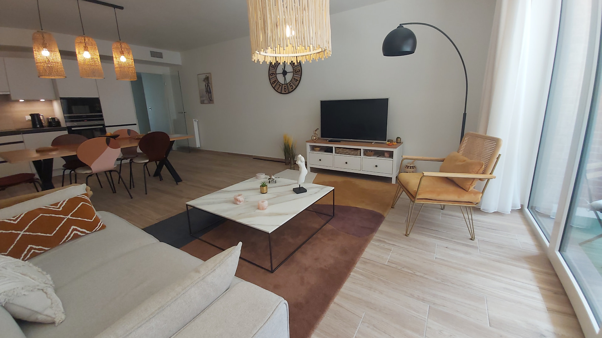 Grand angle du séjour du Courbevoie lodge : canapé écru, fauteuil ocre, tapis à motifs et baie vitrée